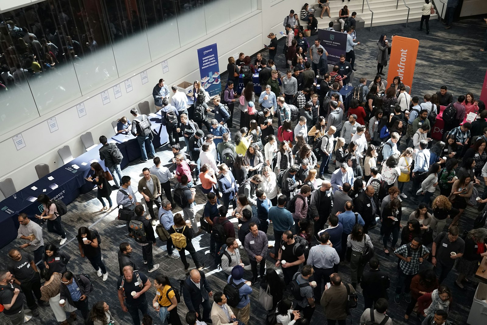 Crowded exhibition hall seen from above, with rows of visitors walking between booth counters and banners