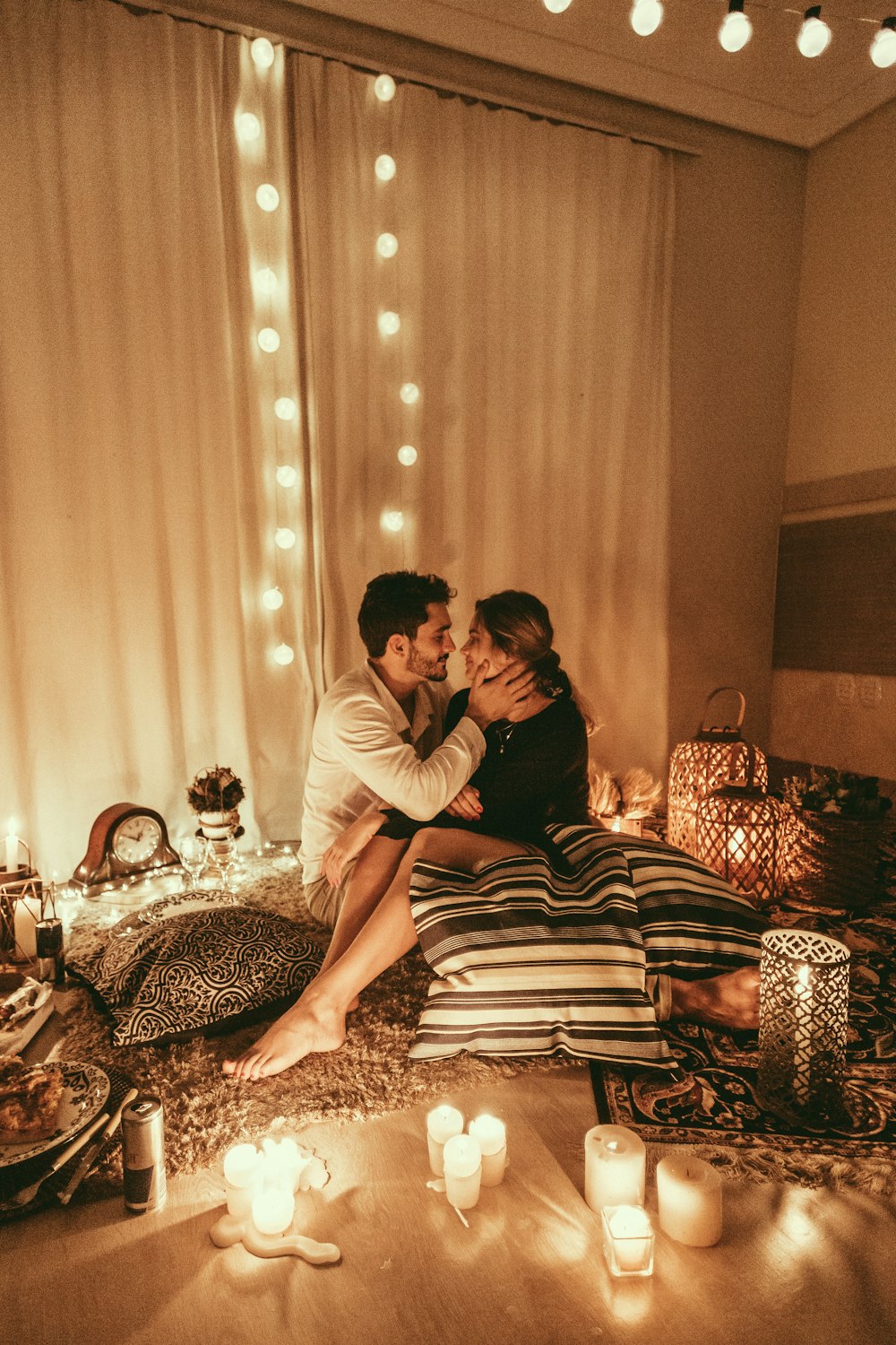 homem e mulher sentados no chão e prestes a se beijar com velas acesas dentro da sala