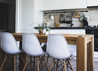 brown wooden dining table with white chairs near kitchen