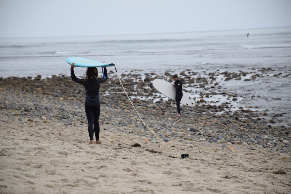 person carrying blue surfboard on beach