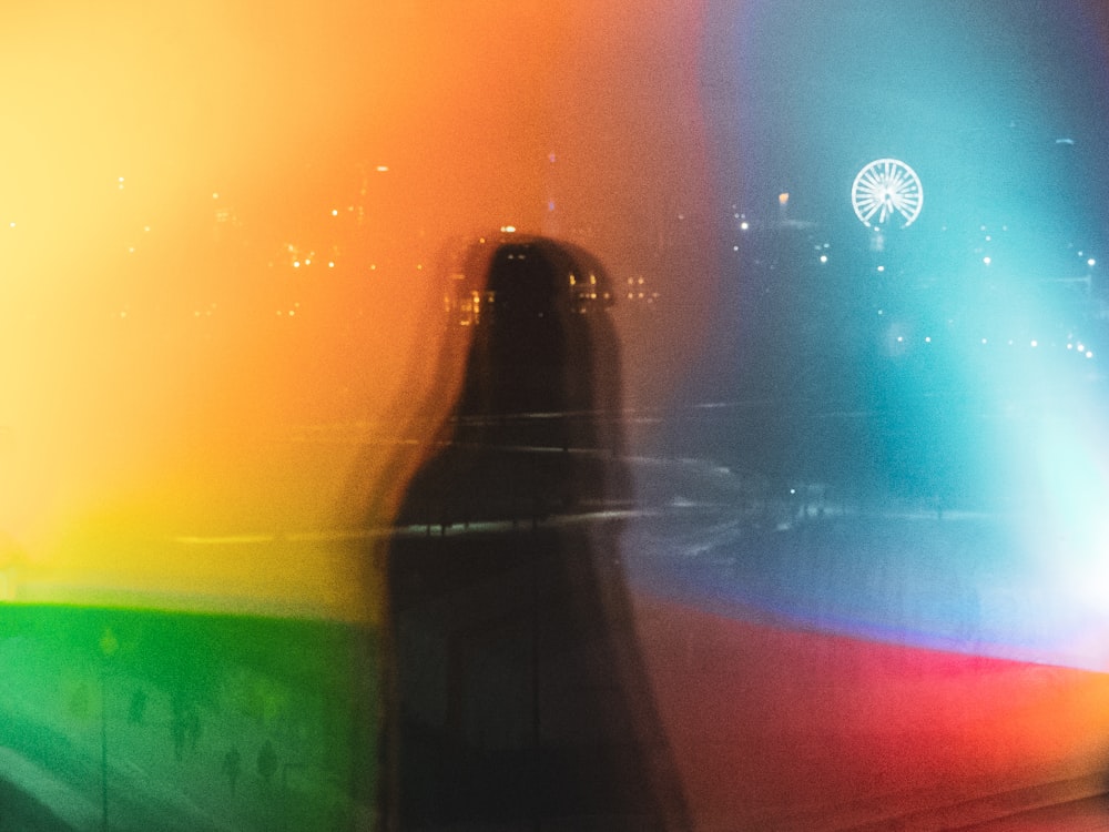 a blurry photo of a person standing in front of a rainbow light