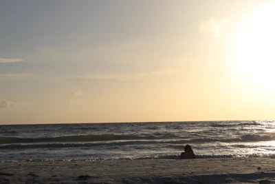 Sunset over a serene beach with a lone traveler sitting on the sand, reflecting.