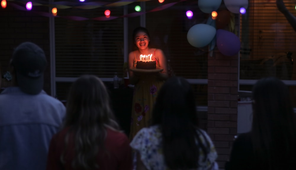 people watching women holding a cake close-up photography