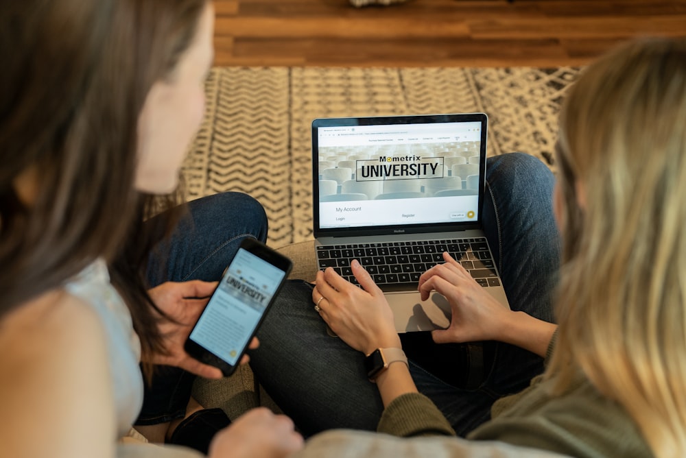 woman using laptop sitting beside woman holding smartphone