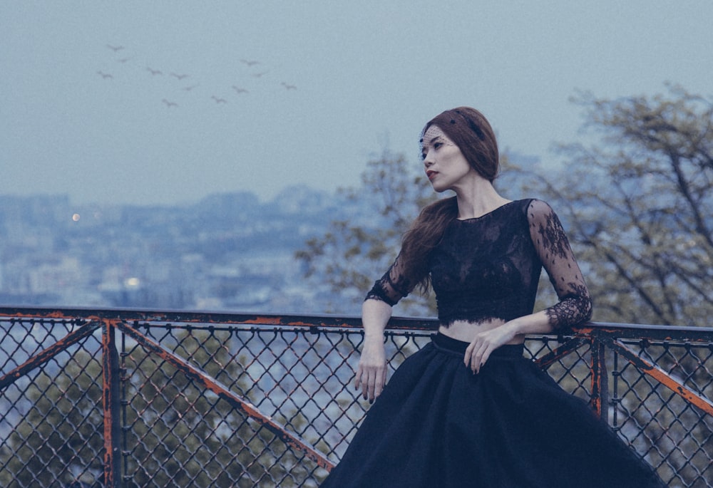 woman wearing black laced ballgown standing beside black mesh-link fence