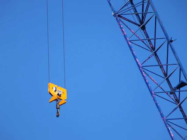 A powerful yellow crane lifting heavy steel beams against a clear sky.