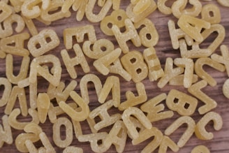 A close-up view of uncooked alphabet pasta scattered randomly on a wooden surface.