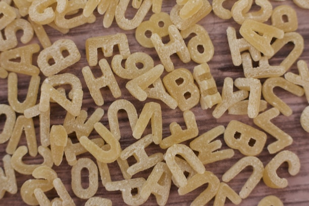 A close-up view of uncooked alphabet pasta scattered randomly on a wooden surface.