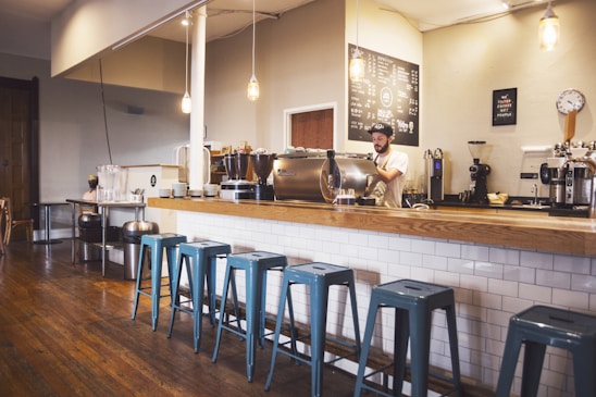 Cozy vintage coffee shop interior with green walls, wooden tables, and a barista preparing a specialty coffee.