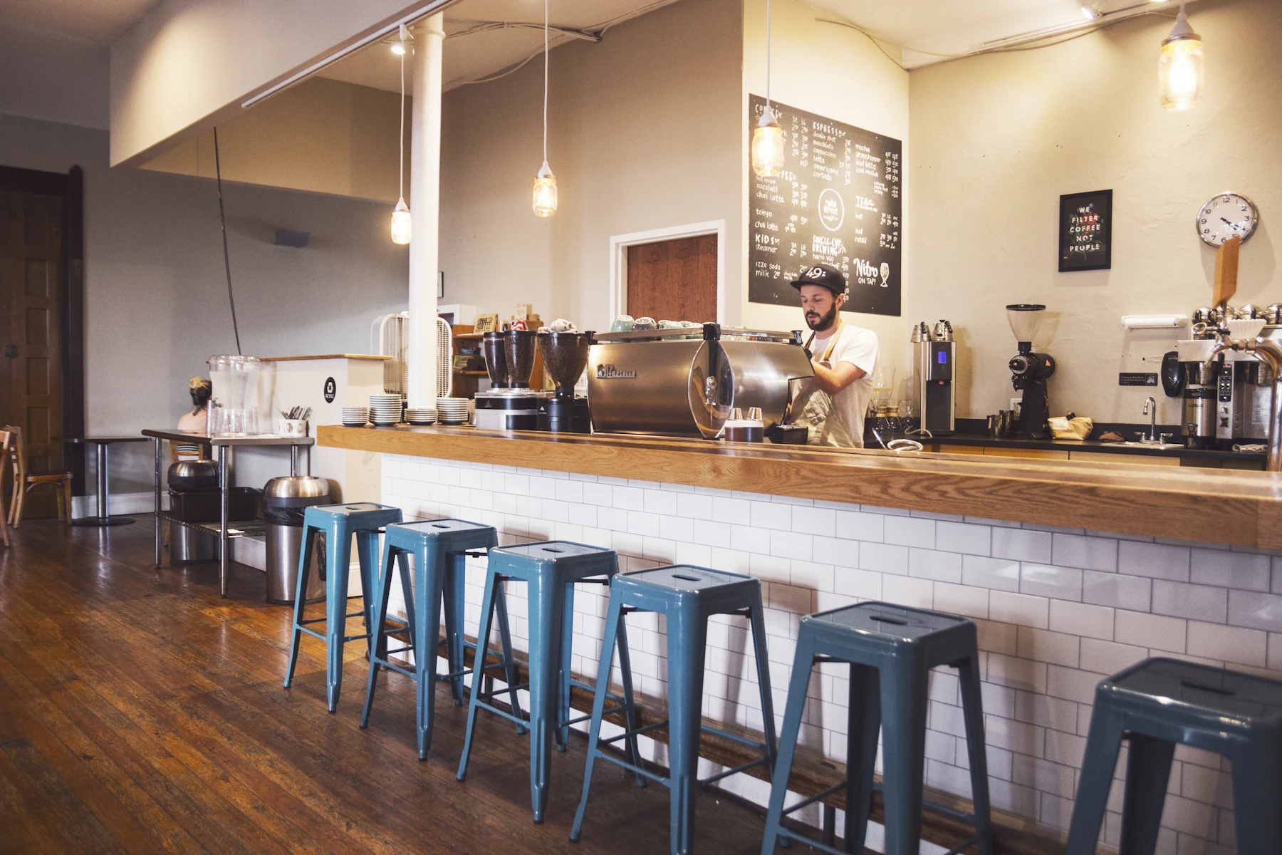 A specialty espresso bar: a timber counter, stools, a barista working behind the machine.