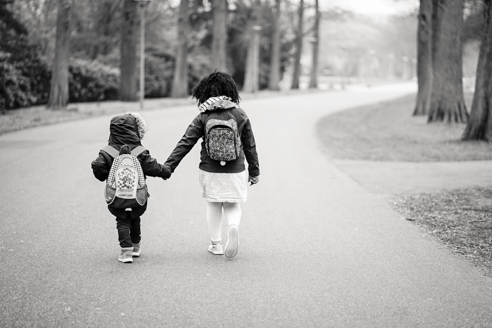 grayscale photography of two toddlers walking on road