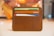 A brown leather wallet is holding several credit and payment cards. The wallet is neatly sewn and sits on a light surface with a warm, blurred background. The cards are of various colors, prominently featuring names of financial services.