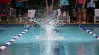 Wide shot of a swimming pool with athletes diving in, water splashing energetically.