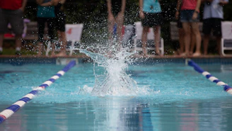 Wide shot of a swimming pool with athletes diving in, water splashing energetically.