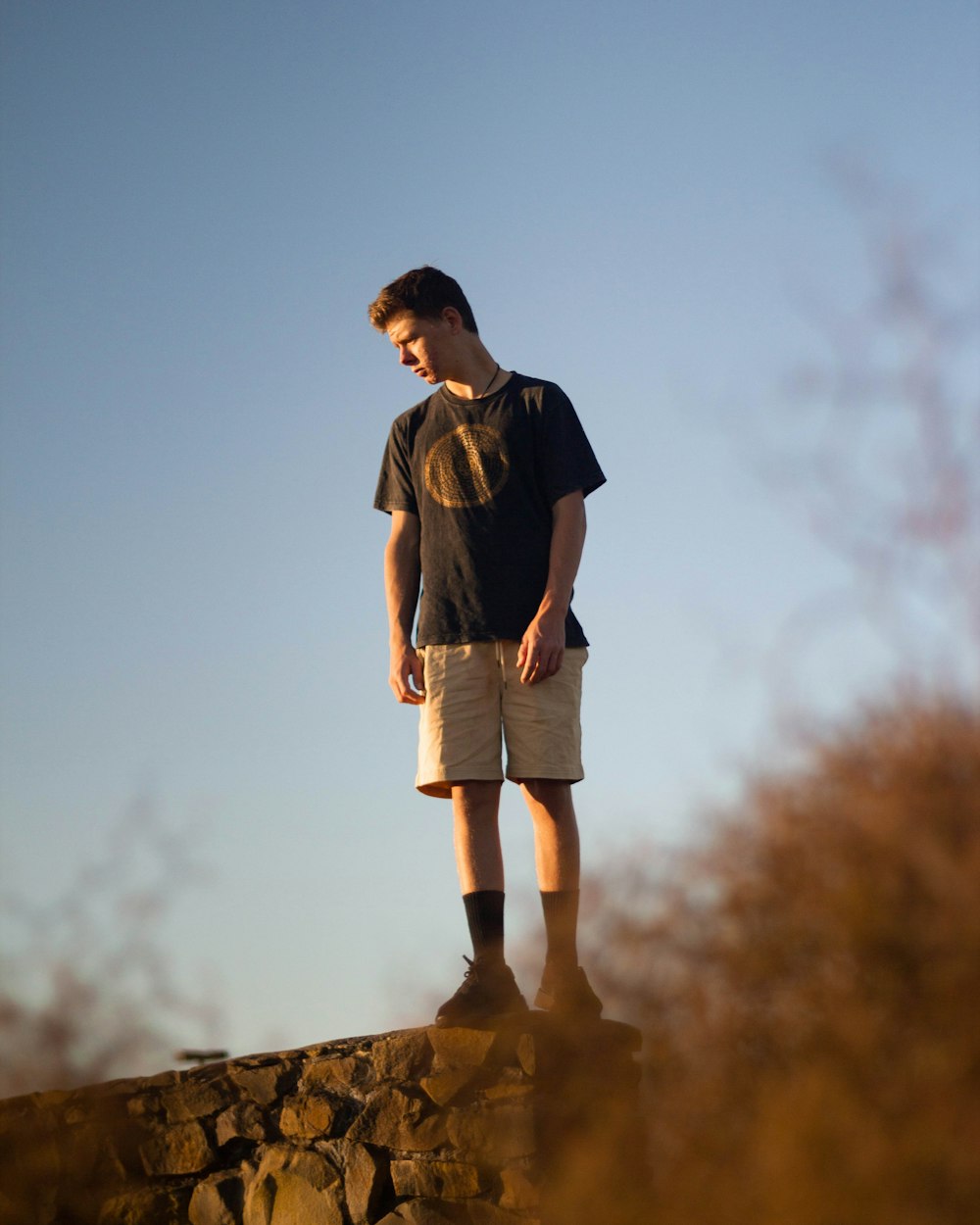 man in black t-shirt and beige shorts standing on rocks