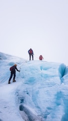 Several climbers are ascending an ice-covered slope, using ropes and climbing gear. The environment is stark and chilly, with expansive vistas of ice stretching into the horizon.