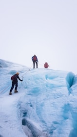 Group of climbers roped together ascending a steep glacier under a clear blue sky.
