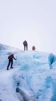 Several climbers are ascending an ice-covered slope, using ropes and climbing gear. The environment is stark and chilly, with expansive vistas of ice stretching into the horizon.