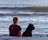 girl and dog sitting on seashore while watching on sea