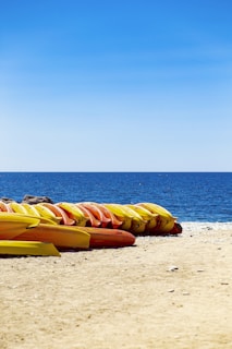 A serene view of kayaks and paddleboards lined up on a sandy beach.