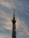 A tall communication tower stands against a backdrop of soft, wispy clouds in a sky tinged with shades of blue and gray. The structure is equipped with various antennas and satellite dishes.