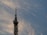 A tall metal communication tower extends into the sky, featuring various antennas and satellite dishes. The backdrop is a sky filled with soft, wispy clouds that catch the golden hues of the setting sun.
