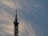 A tall metal communication tower extends into the sky, featuring various antennas and satellite dishes. The backdrop is a sky filled with soft, wispy clouds that catch the golden hues of the setting sun.