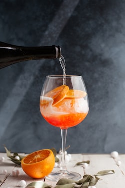 Vibrant orange Aperol Spritz served in a large wine glass with ice, a fresh orange slice, and green olive garnish on a sunlit patio table