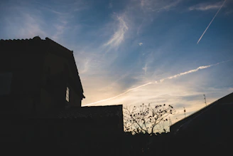 Modern house silhouette against a sunset by Šiaulių lake, surrounded by natural greenery.