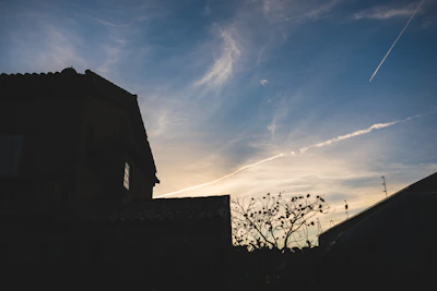 Modern house silhouette against a sunset by Šiaulių lake, surrounded by natural greenery.
