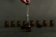 Close-up of botanical extracts dripping from a glass dropper into a small amber bottle.