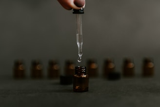 Close-up of amber fragrance oil drops falling into a glass bottle on a wooden table.