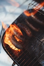 Close-up of sizzling bratwurst on a charcoal grill with flames