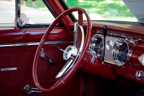 A vintage car interior with a red steering wheel and dashboard. Chrome details highlight the dashboard instruments and controls, while the leather upholstery enhances the classic aesthetic.