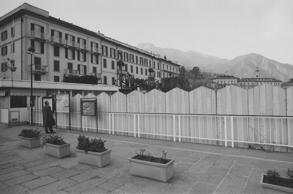 grayscale photography of man standing beside fence during daytime