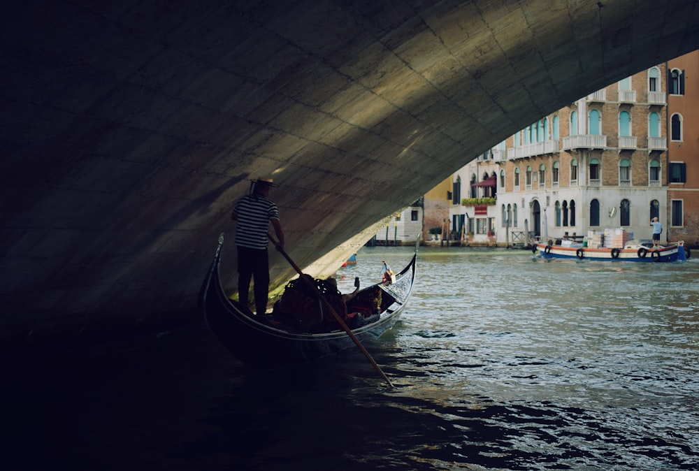 man riding boat under bridge during daytime