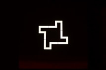 A geometric, luminescent pattern creating a maze-like shape against a dark background. The shape consists of straight lines forming right angles, reminiscent of a glowing path or digital design.
