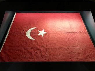 A large red flag is displayed, featuring a white crescent moon and a five-pointed star in the center. The fabric shows some wrinkles and texture, indicating its material and age.