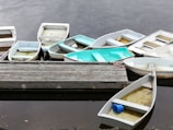 Buckets of colorful marine paint lined up on a dock beside various watercraft.