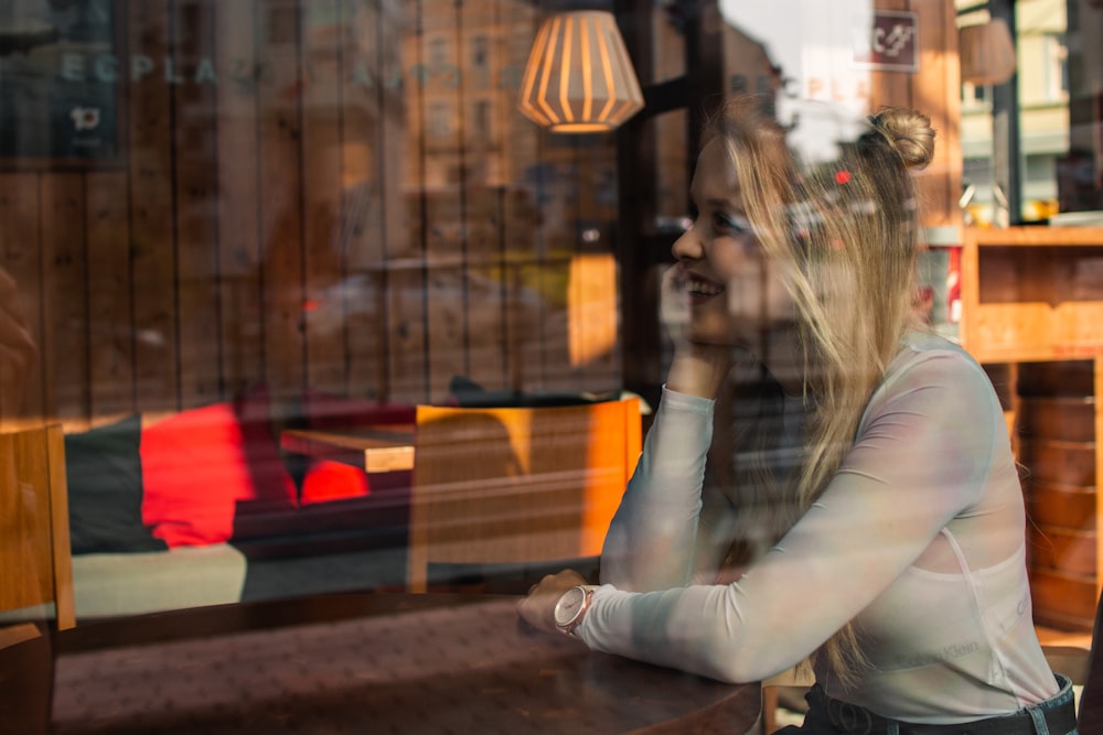 woman sitting beside table near glass smiling