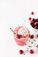 Vertical image of a rich cherry and blueberry smoothie topped with fresh berries and a straw.