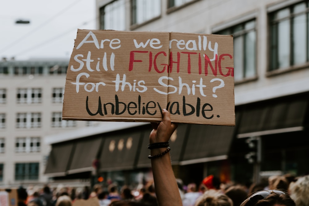 person raising are we really still fighting for this shit? unbelievable sign near people and building