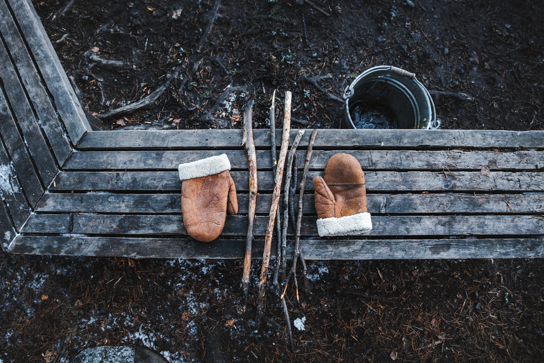 A pair of leather mitts and a few cut sticks laid on a plank bench, seen from above