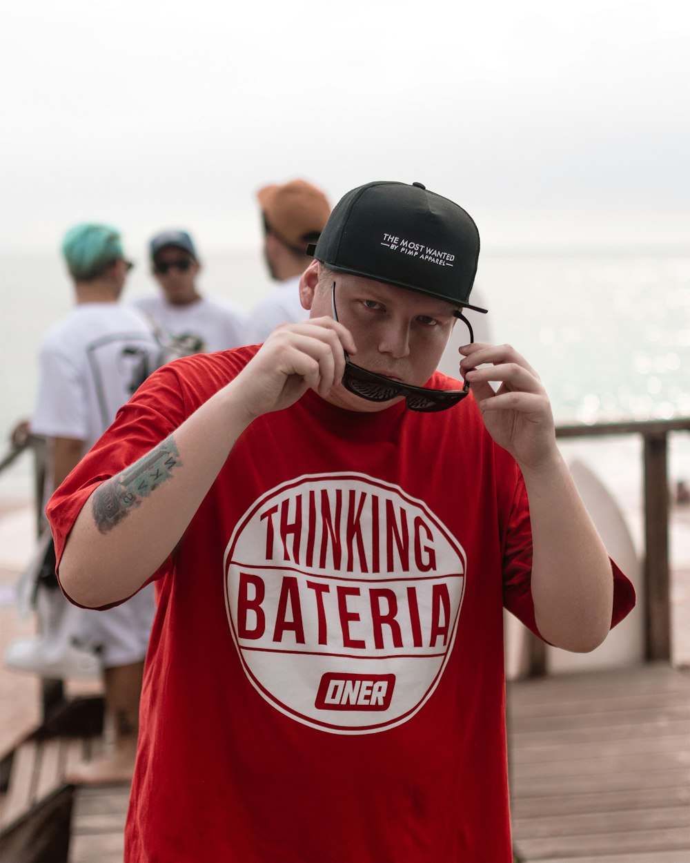 man wearing white and black crew-neck shirt and black wayfarer sunglasses standing on brown wooden boardwalk