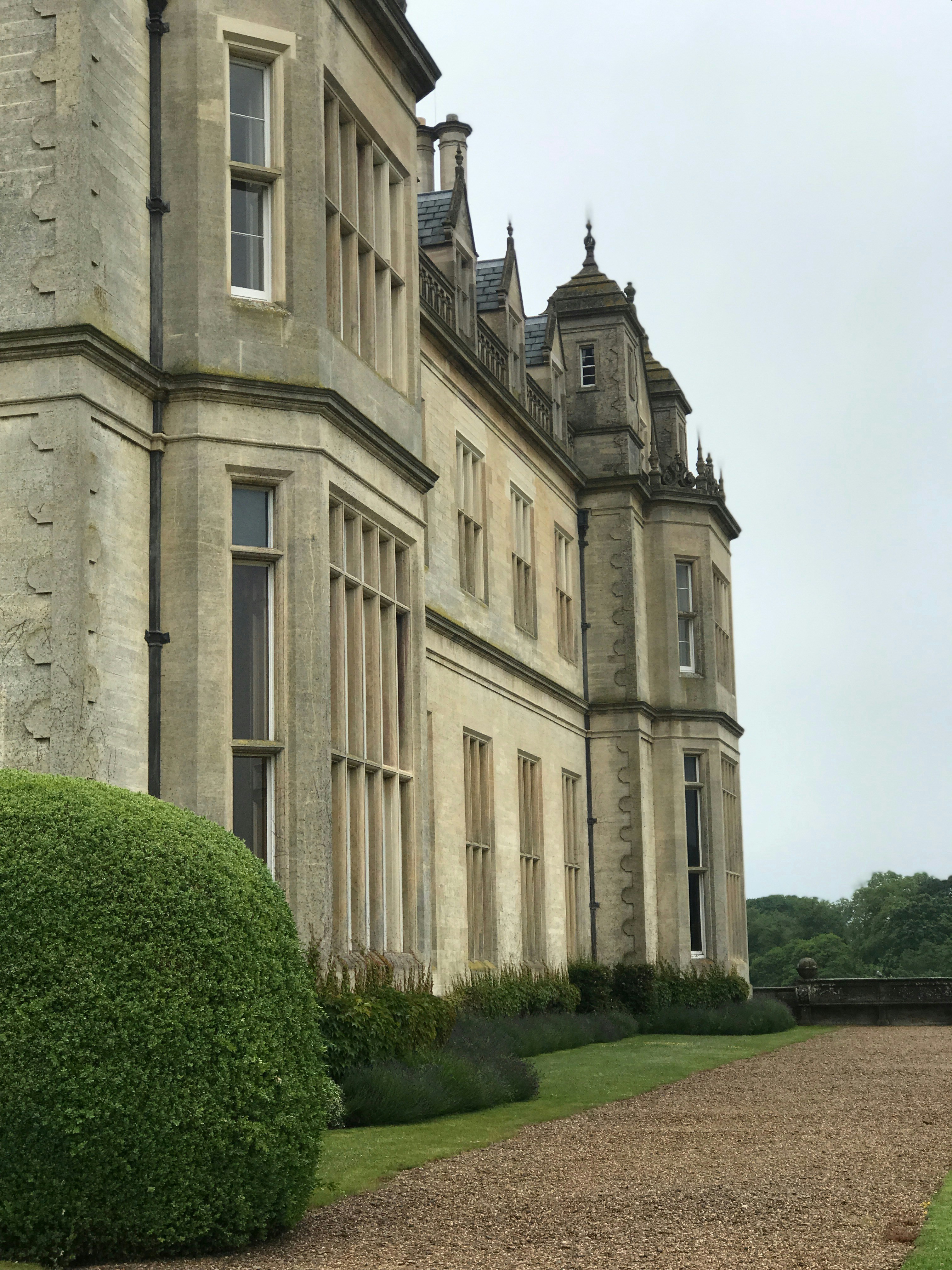 Stately English manor hotel exterior, stone facade, formal gardens, overcast sky, muted palette