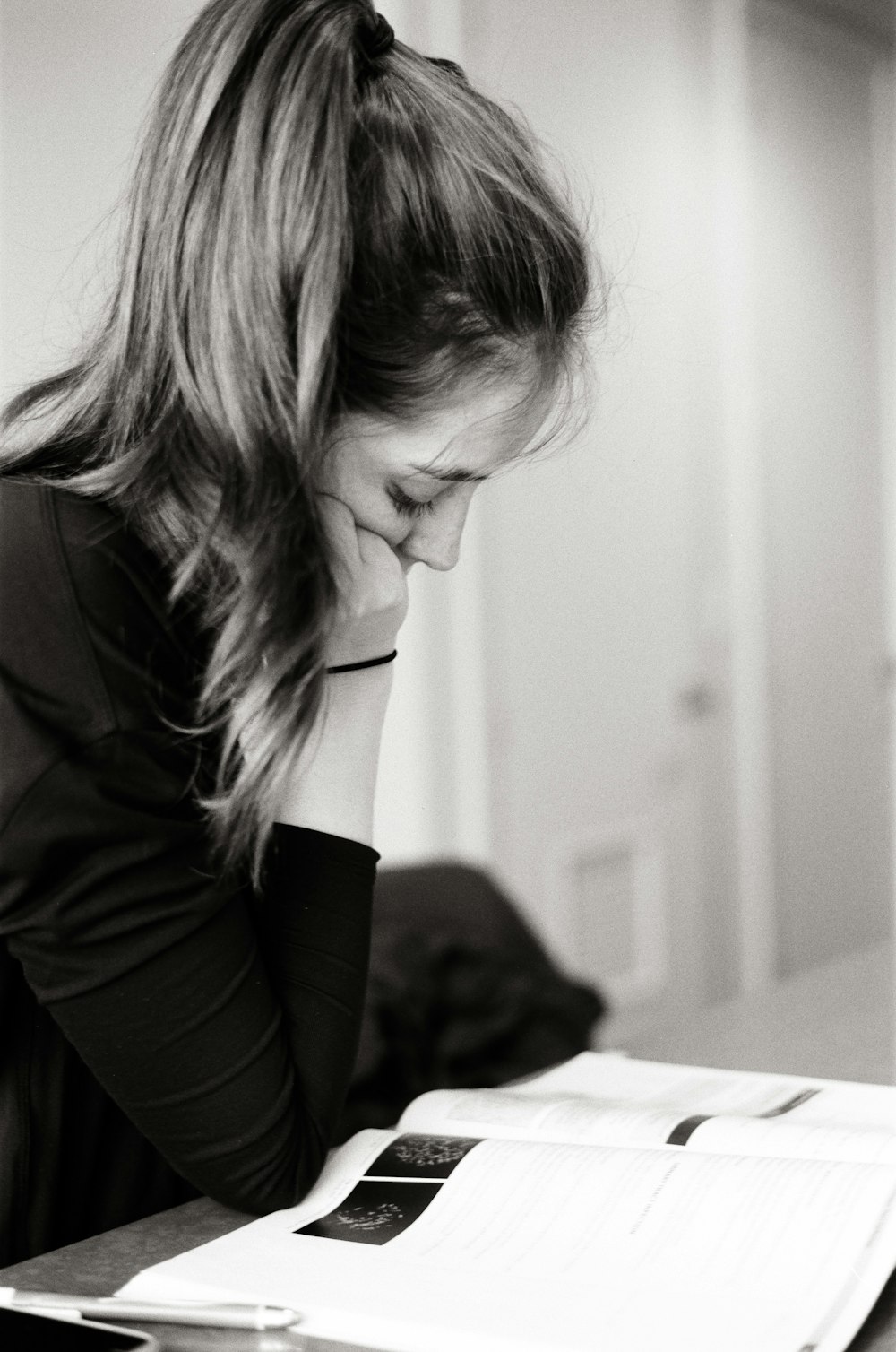 woman resting her head on her right hand beside table with opened book