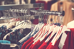 A clothing rack filled with various garments on hangers, with a prominent display of red and floral patterns. The focus is on neatly organized clothes in a retail setting, highlighting the variety and arrangement.