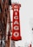 A vertical red sign attached to a building displays the word 'CHICAGO' in large, illuminated letters. The sign is ornate with intricate details and is positioned against a backdrop of urban architecture, including modern skyscrapers and an older brick building with decorative elements.