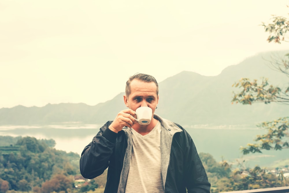 man drinking from mug while standing on deck