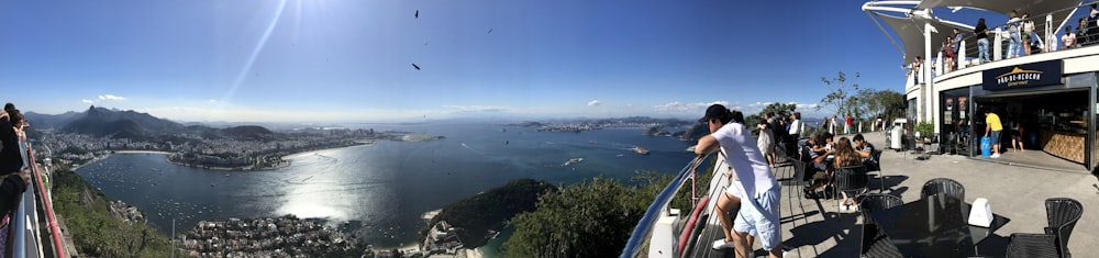 panorama photography of man standing beside railing overlooking city